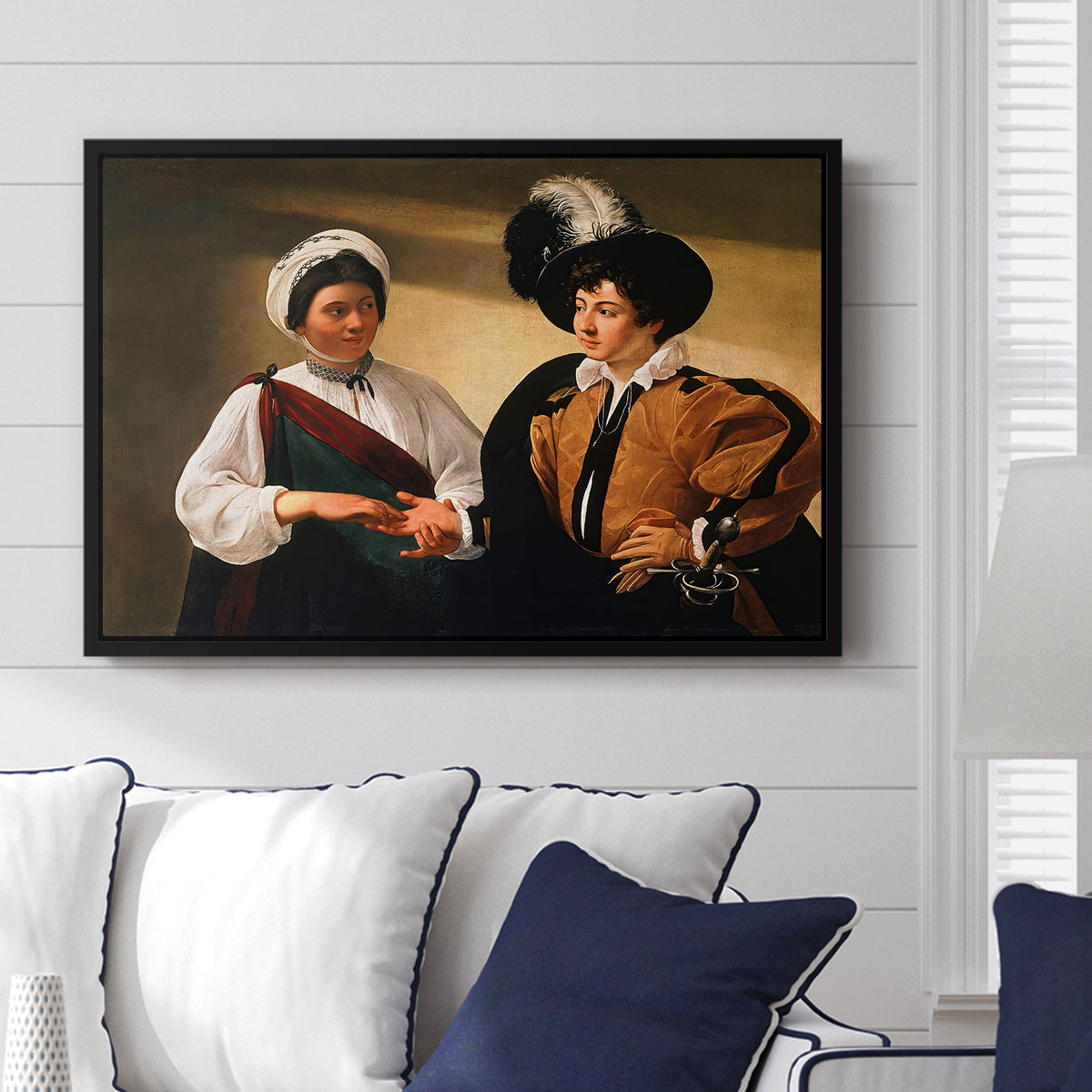 The Fortune Teller (Louvre Version), c. 1595 by Caravaggio displayed above a sofa in a living room in a black floater frame, featuring a fortune teller examining hand of man as she slyly removes his ring.