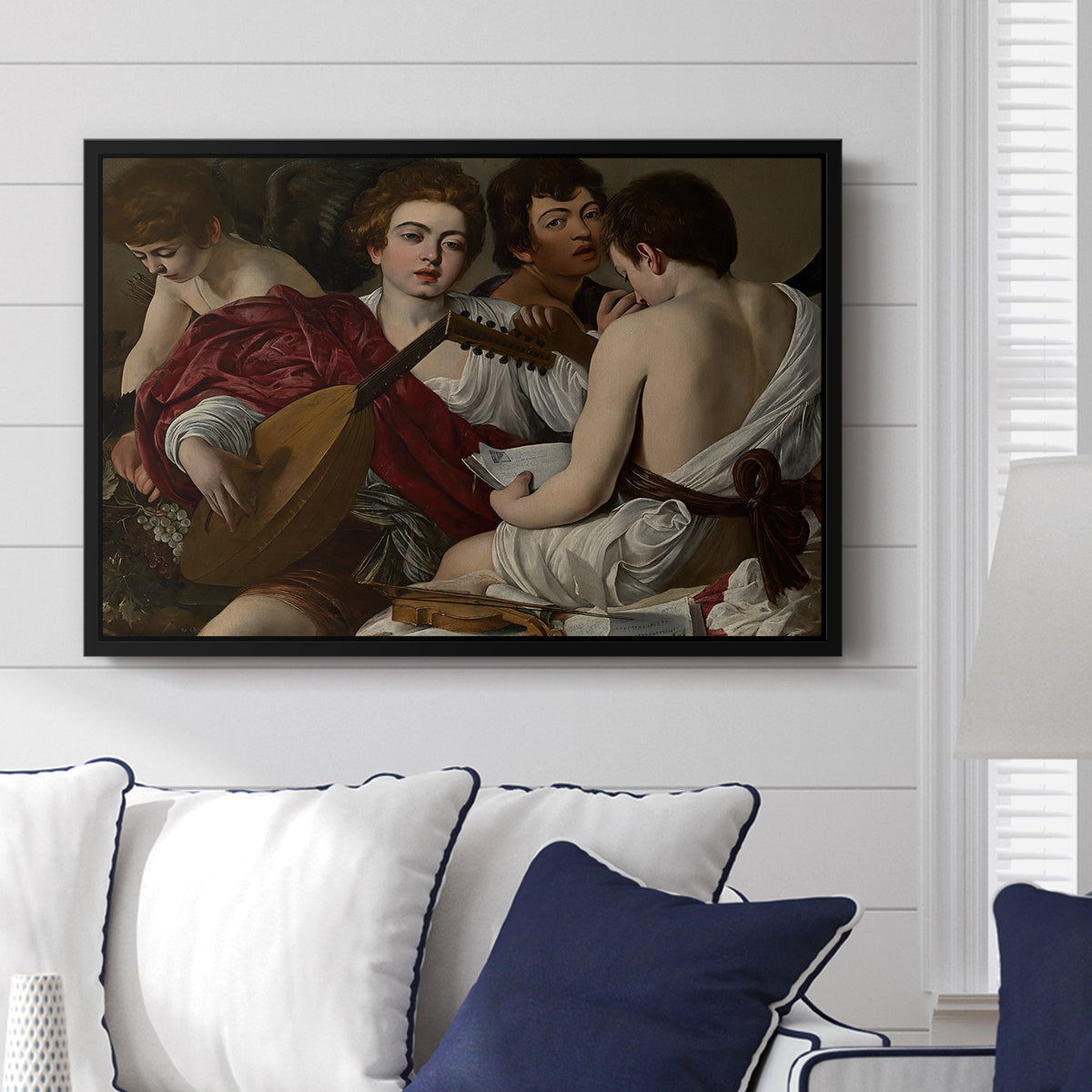 The Musicians, c. 1595 by Caravaggio displayed above a sofa in a living room in a black floater frame, featuring an ensemble of musicians holding lute and singing in close arrangement.