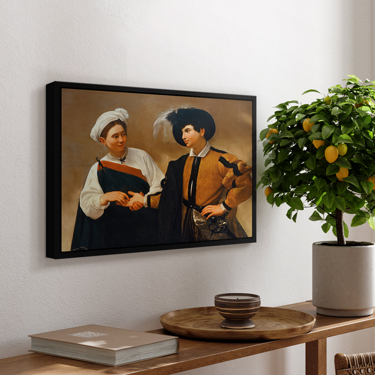 The Fortune Teller (Capitoline Version), c. 1599 by Caravaggio, presented in a black floater framed canvas featuring a woman reading man's palm while discreetly removing his ring, displayed above a hallway console table.