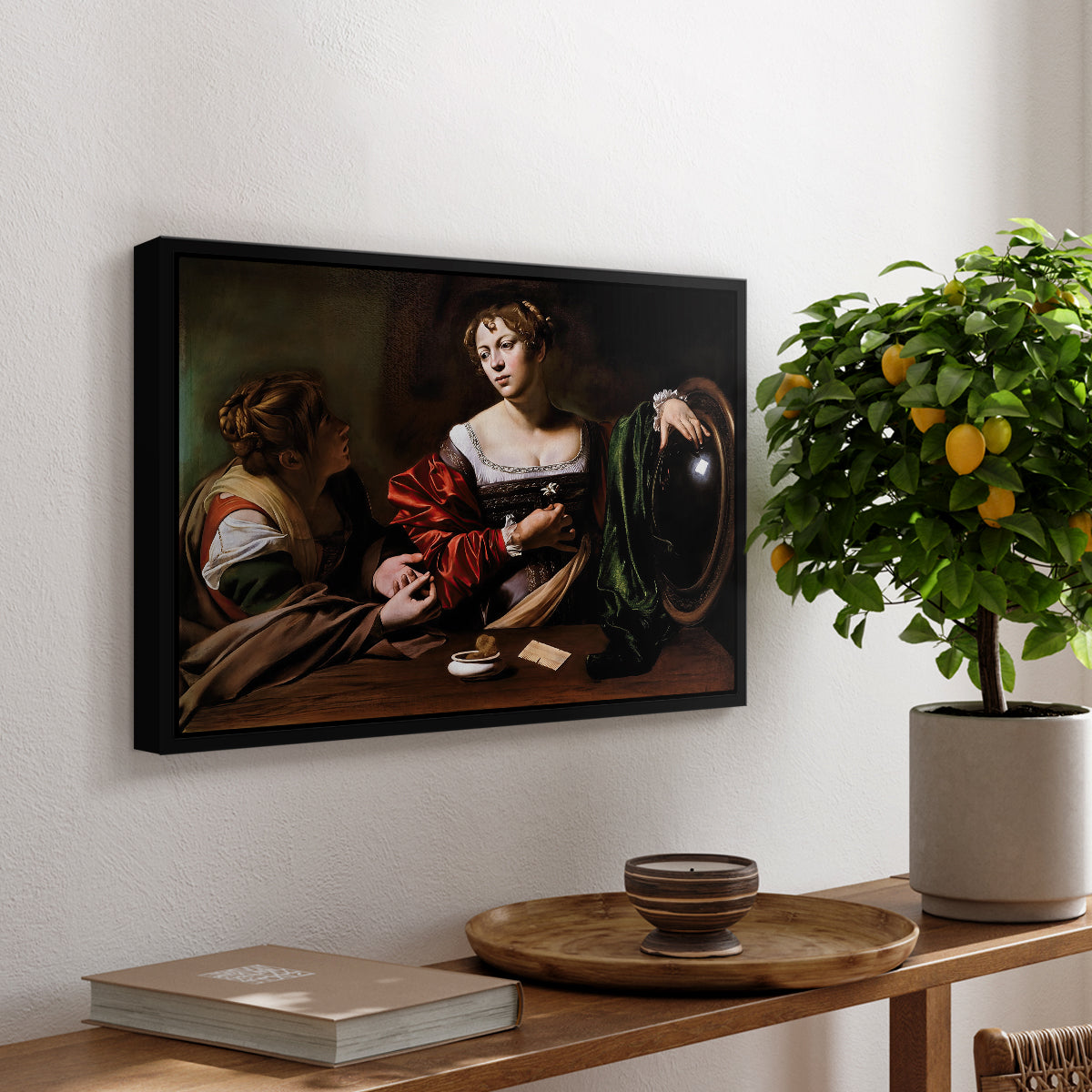 Martha and Mary Magdalene, c. 1598 by Caravaggio, presented in a black floater framed canvas featuring a two women seated together in conversation with symbolic objects on table, displayed above a hallway console table.