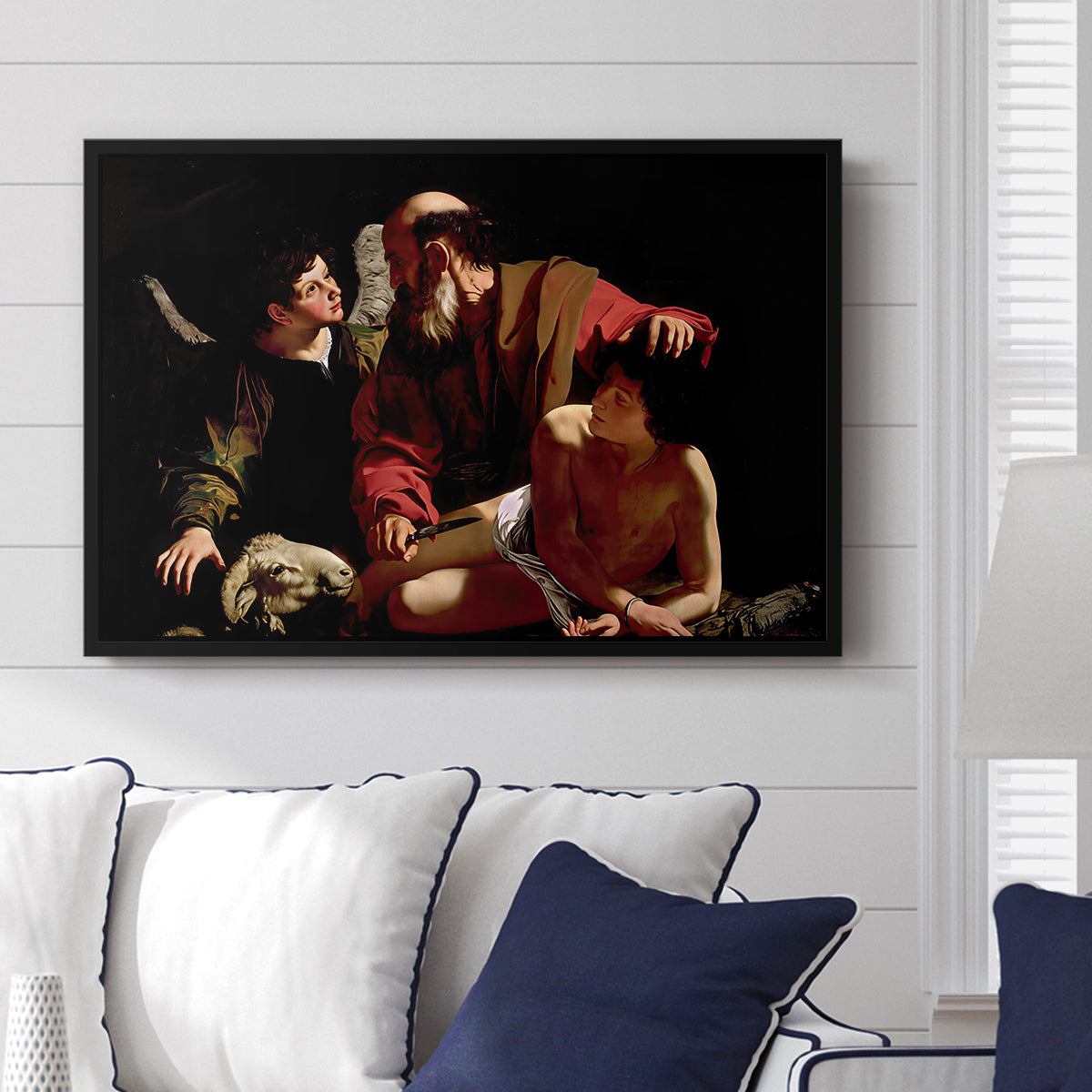 The Sacrifice of Isaac (Uffizi Version), c. 1603 by Caravaggio displayed above a sofa in a living room in a black floater frame, featuring a biblical scene of father about to sacrifice son as angel restrains him.