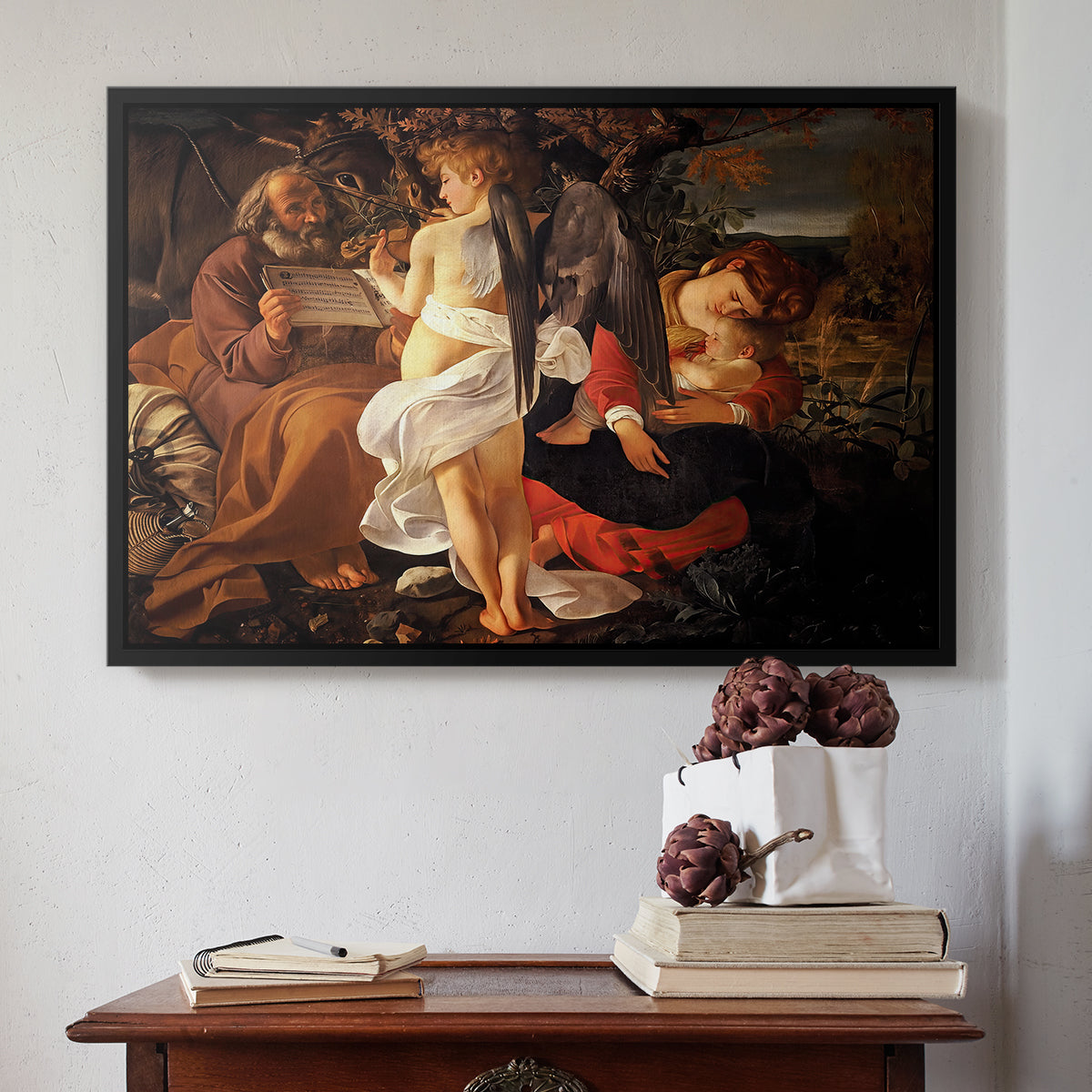 Black floater framed canvas featuring Rest on the Flight into Egypt, c. 1597 by Caravaggio above an entryway table in a minimalist foyer.