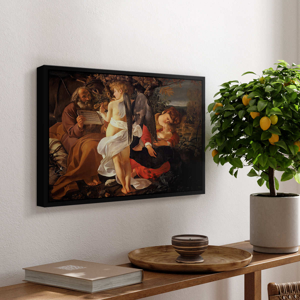 Rest on the Flight into Egypt, c. 1597 by Caravaggio, presented in a black floater framed canvas featuring the Holy Family resting in landscape with angel playing violin, displayed above a hallway console table.