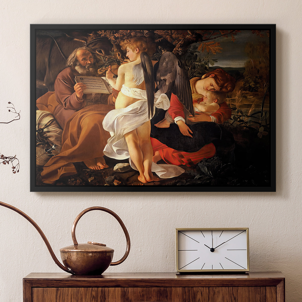 Black floater framed canvas featuring a peaceful religious moment with figures reclining in natural setting, displayed above a cabinet in a soft-toned living room.