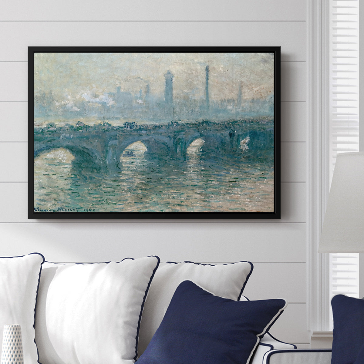 Waterloo Bridge, Gray Weather, 1900 by Claude Monet displayed above a sofa in a living room in a black floater frame, featuring an impressionist cityscape with bridge fading into fog over water.