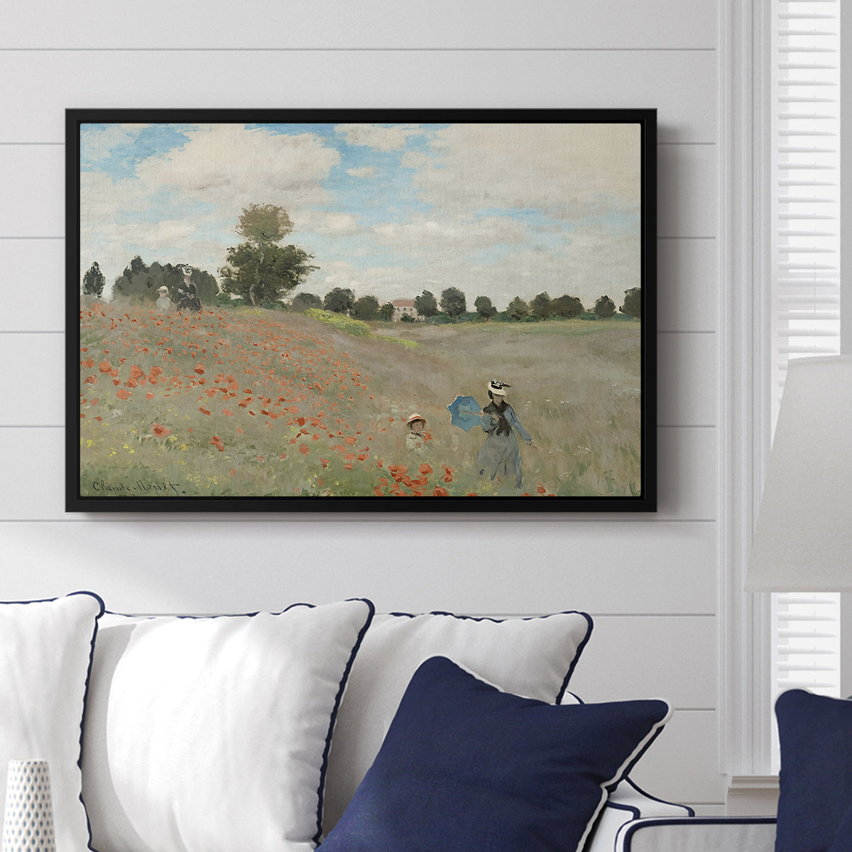 The Poppy Field near Argenteuil, 1873 by Claude Monet displayed above a sofa in a living room in a black floater frame, featuring an impressionist countryside scene with flowers and strolling figures.