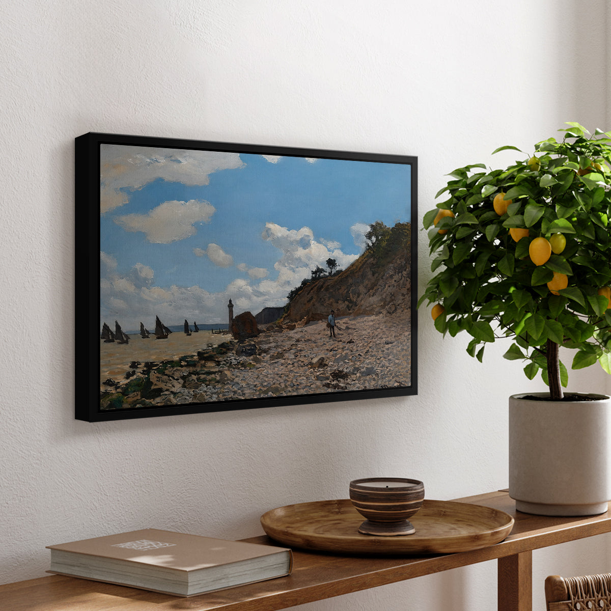 The Beach at Honfleur, 1864 by Claude Monet, presented in a black floater framed canvas featuring a coastal beach scene with figures gathered along shoreline and boats nearby, displayed above a hallway console table.