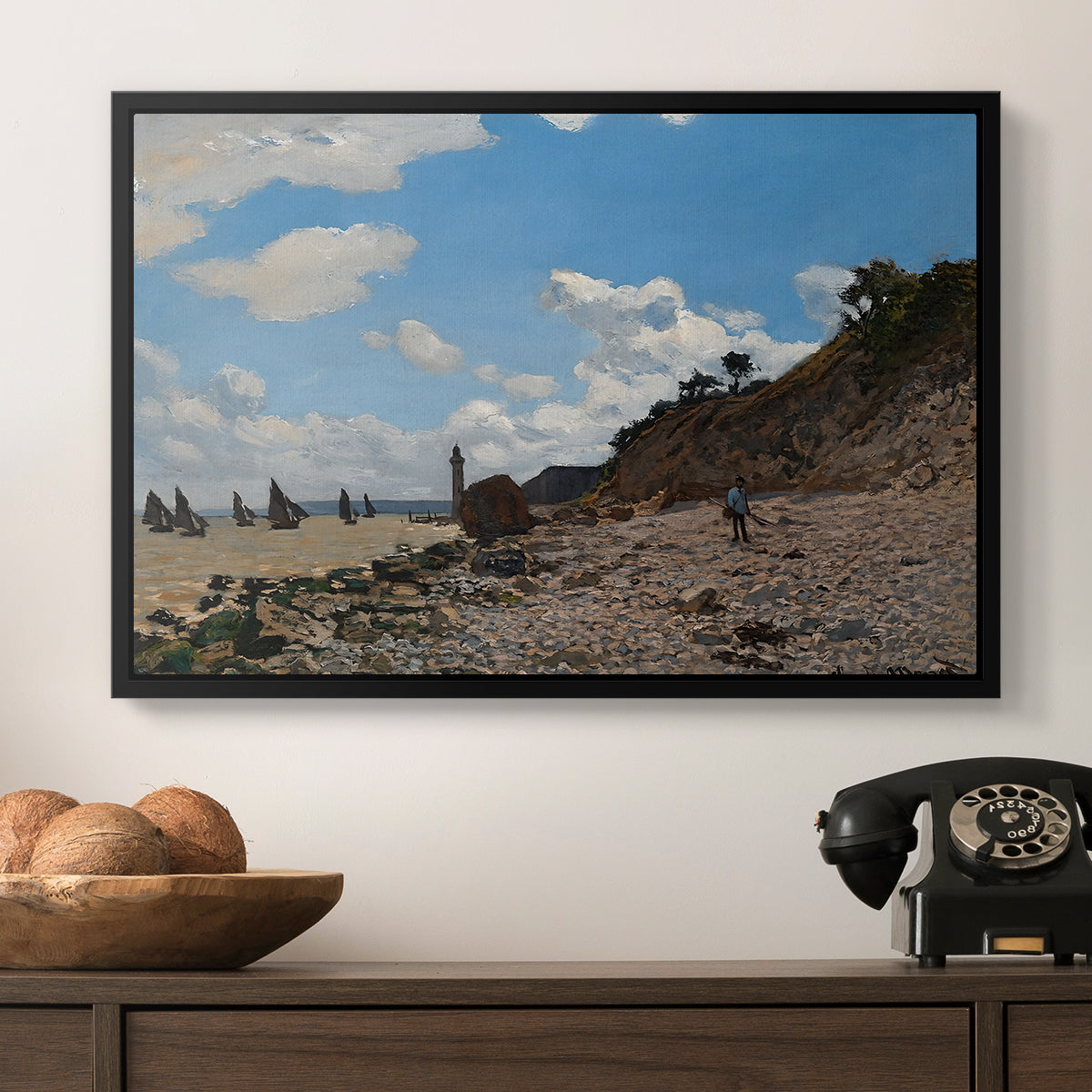 The Beach at Honfleur, 1864 by Claude Monet in a black floater framed canvas displayed above a console table in a hallway, featuring a coastal landscape with boats and people along shore.