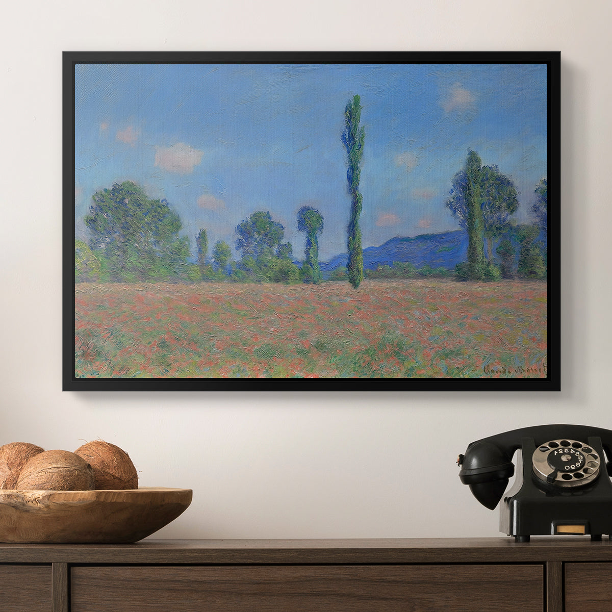Poppy Field (Giverny), 1890-1891 by Claude Monet in a black floater framed canvas displayed above a console table in a hallway, featuring a rural field filled with red blossoms beneath open sky.