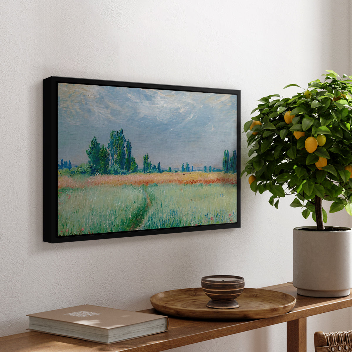 The Wheat Field (Champ de Blé), 1881 by Claude Monet, presented in a black floater framed canvas featuring a golden wheat field stretching across landscape under soft sky, displayed above a hallway console table.