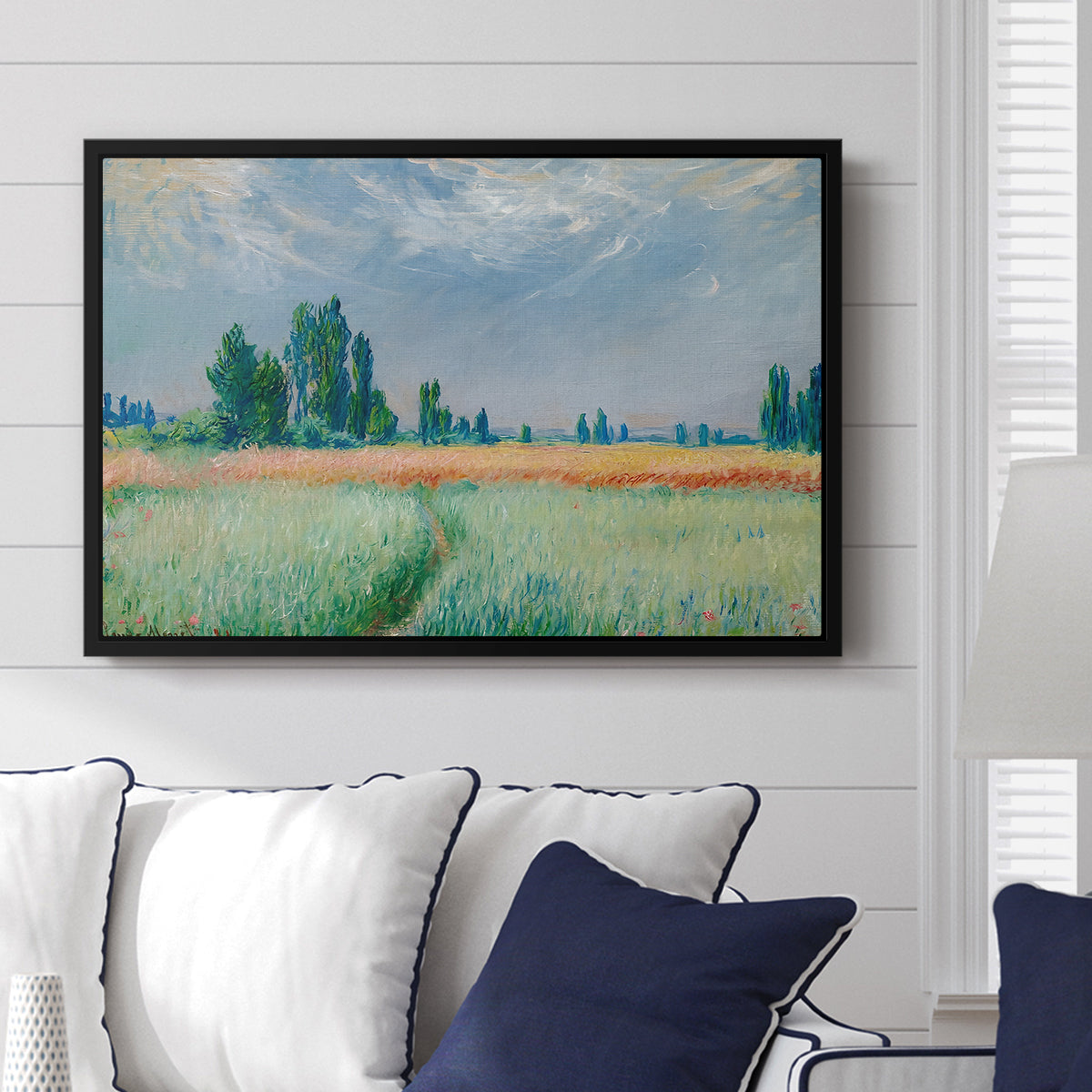 The Wheat Field (Champ de Blé), 1881 by Claude Monet displayed above a sofa in a living room in a black floater frame, featuring an impressionist depiction of ripened grain field in countryside.