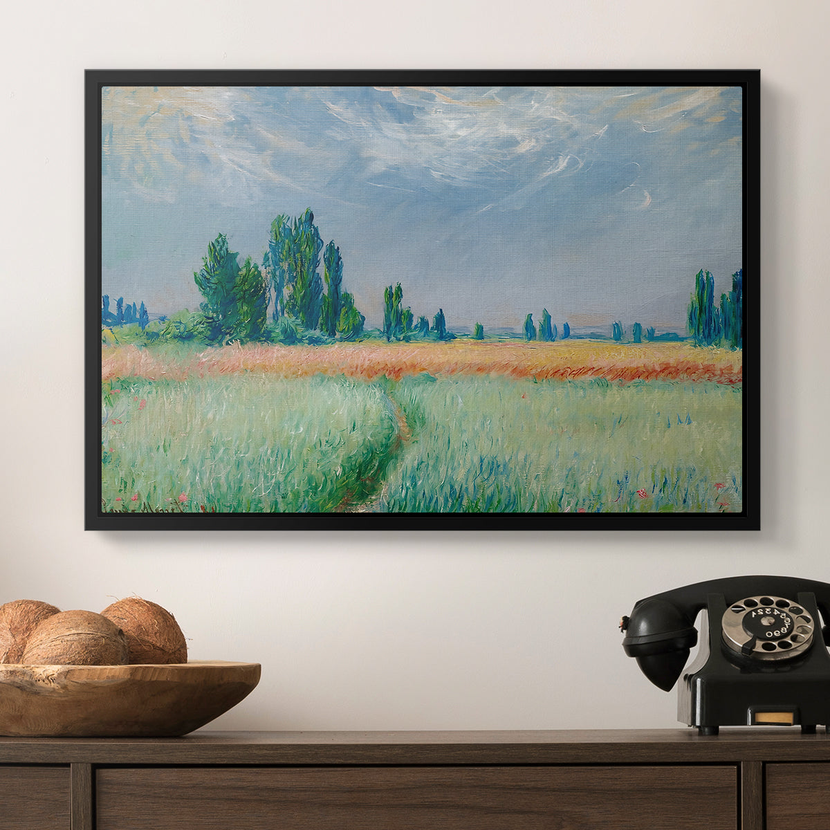 The Wheat Field (Champ de Blé), 1881 by Claude Monet in a black floater framed canvas displayed above a console table in a hallway, featuring a serene rural scene with textured wheat under natural light.