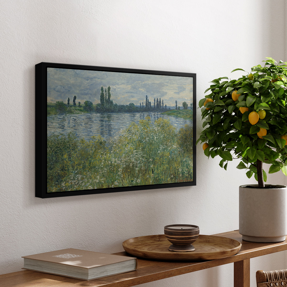 Banks of the Seine, Vétheuil, 1880 by Claude Monet, presented in a black floater framed canvas featuring a riverbank landscape with water, trees, and distant village buildings, displayed above a hallway console table.