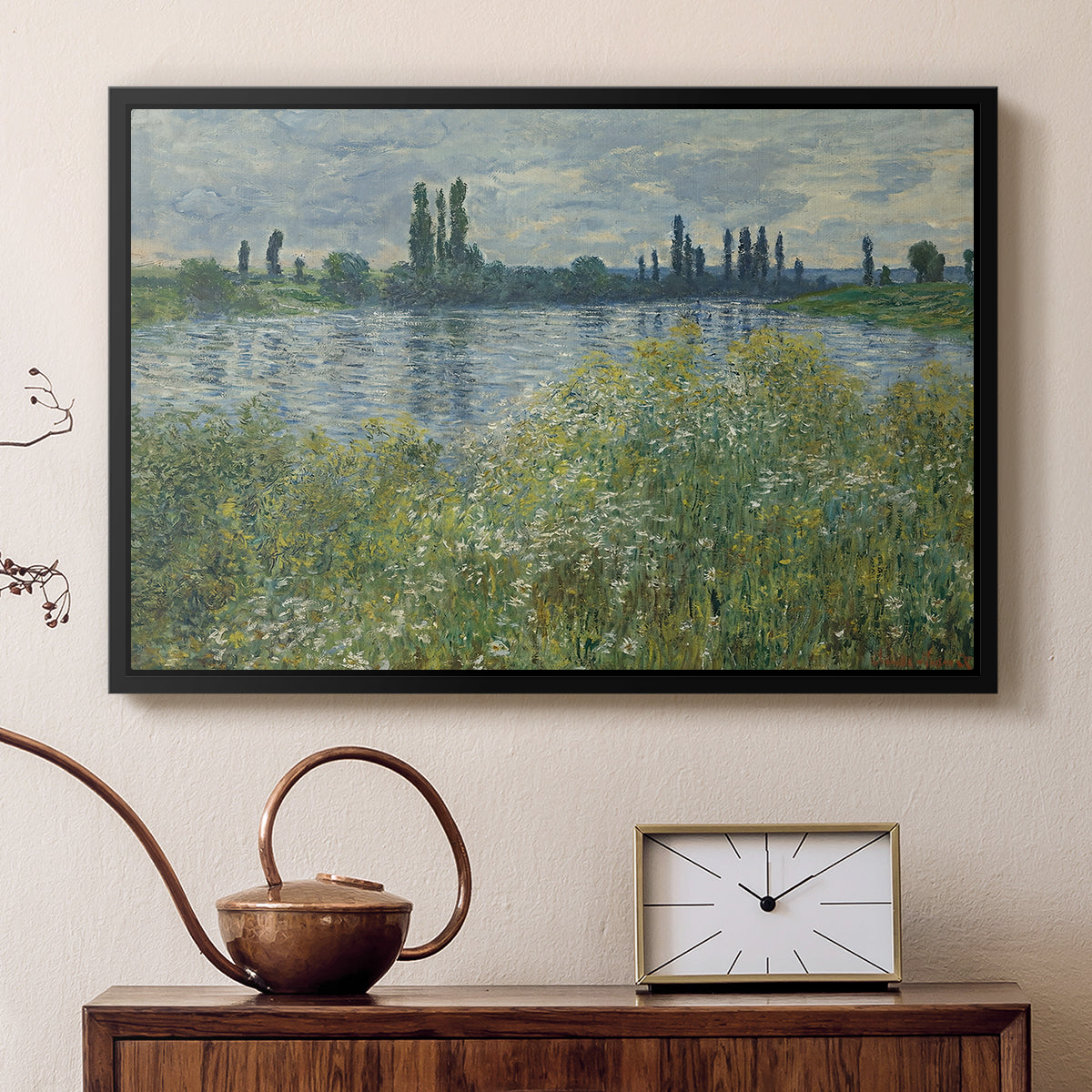 Black floater framed canvas featuring a tranquil riverside scene with houses and vegetation, displayed above a cabinet in a soft-toned living room.