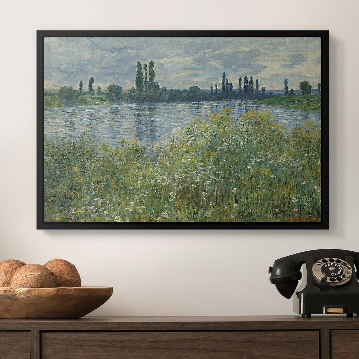 Banks of the Seine, Vétheuil, 1880 by Claude Monet in a black floater framed canvas displayed above a console table in a hallway, featuring a natural landscape with calm water and soft foliage.