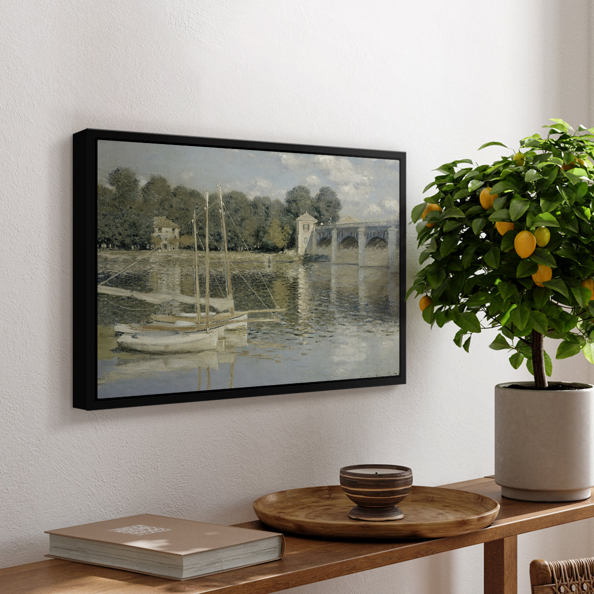 The Bridge at Argenteuil, 1874 by Claude Monet, presented in a black floater framed canvas featuring a bridge spanning river with sailboats and reflections in water, displayed above a hallway console table.