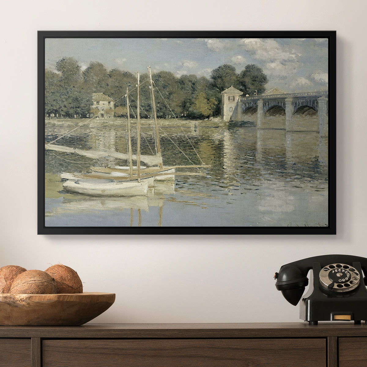 The Bridge at Argenteuil, 1874 by Claude Monet in a black floater framed canvas displayed above a console table in a hallway, featuring a riverside view with architecture and nautical activity.