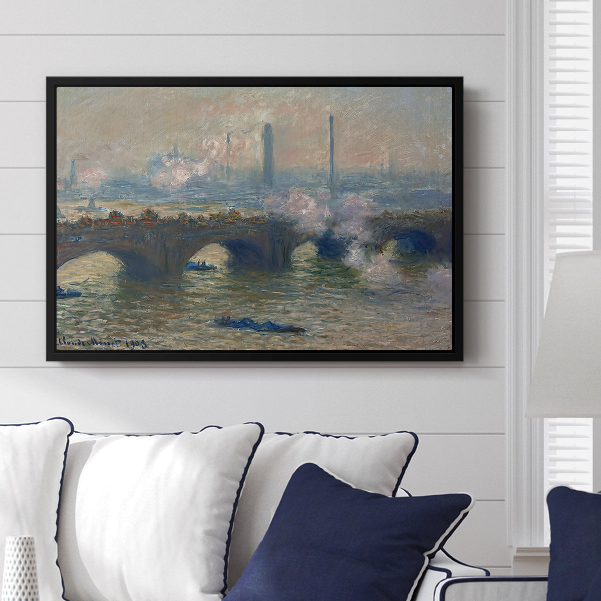 Waterloo Bridge, Gray Day, 1903 by Claude Monet displayed above a sofa in a living room in a black floater frame, featuring an impressionist depiction of bridge with soft gray tones and haze.