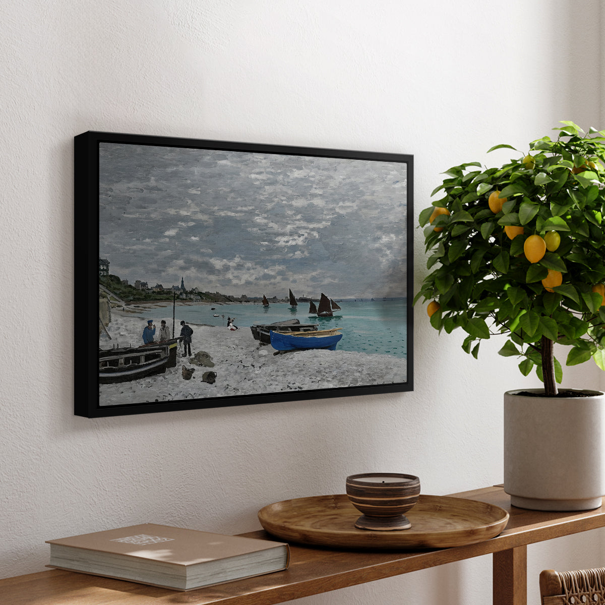 The Beach at Sainte-Adresse, 1867 by Claude Monet, presented in a black floater framed canvas featuring a seaside promenade with figures, flags, and boats along the coast, displayed above a hallway console table.