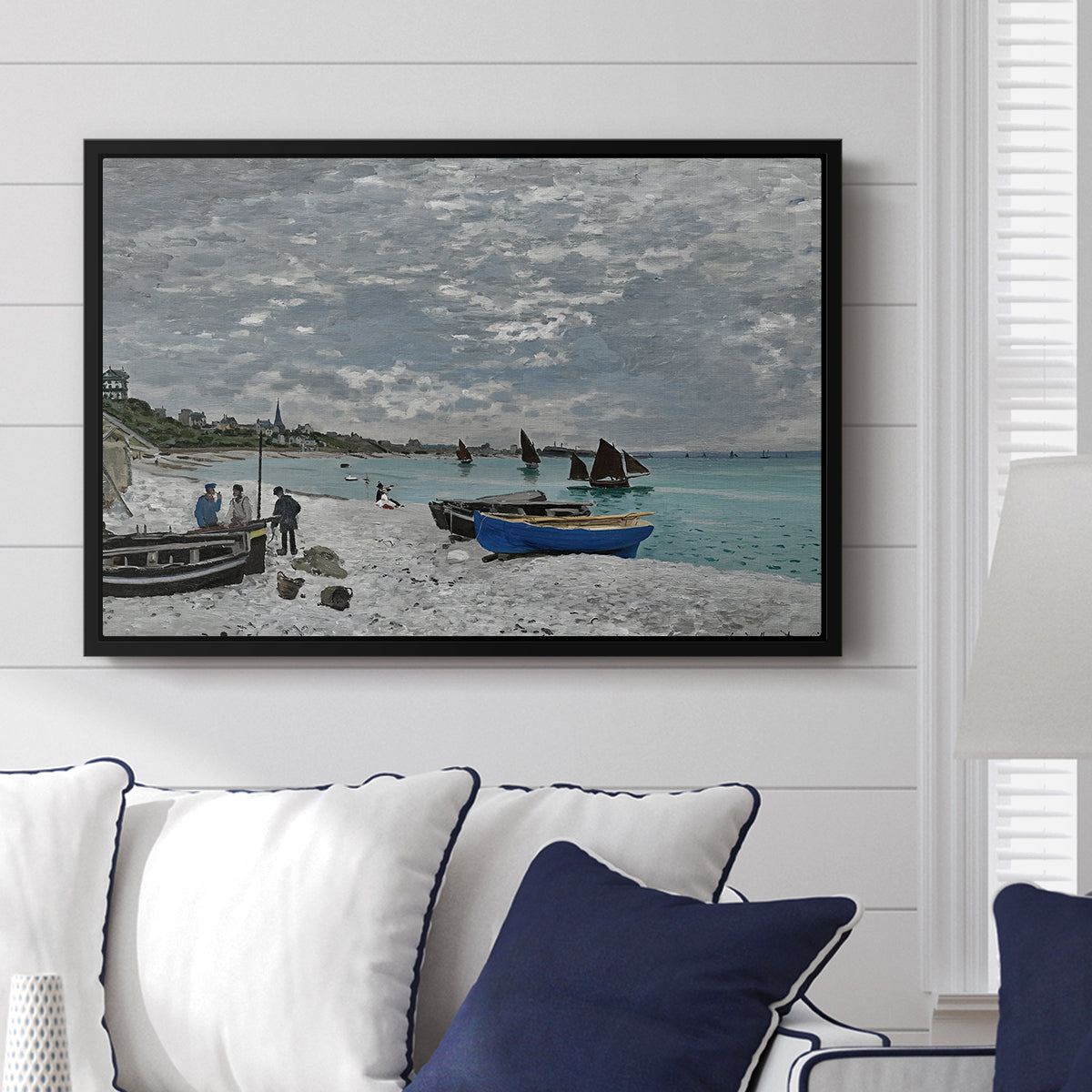 The Beach at Sainte-Adresse, 1867 by Claude Monet displayed above a sofa in a living room in a black floater frame, featuring a lively beach scene with people overlooking water and ships.