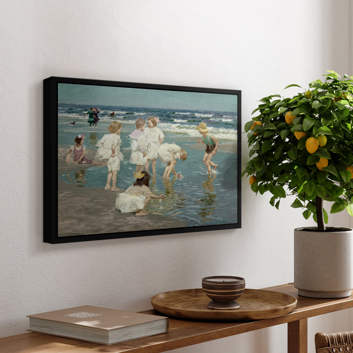 A Holiday, c. 1915 by Edward Henry Potthast, presented in a black floater framed canvas featuring people relaxing and wading in shallow ocean water along a sunny beach, displayed above a hallway console table.