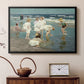 Black floater framed canvas featuring an impressionist coastal view of families enjoying seaside water, displayed above a cabinet in a soft-toned living room.
