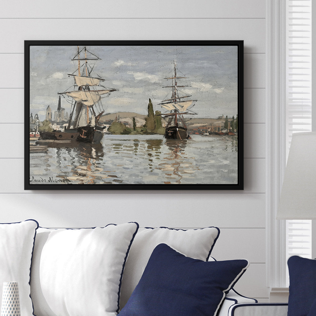Ships Riding on the Seine at Rouen, 1872 by Claude Monet displayed above a sofa in a living room in a black floater frame, featuring an impressionist river scene with anchored sailing ships and reflections.