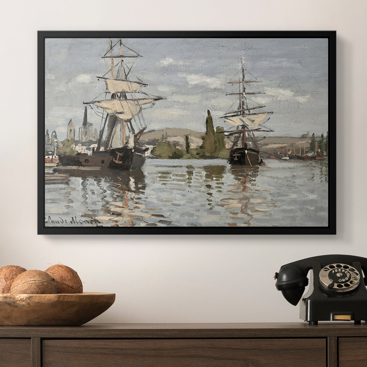 Ships Riding on the Seine at Rouen, 1872 by Claude Monet in a black floater framed canvas displayed above a console table in a hallway, featuring a nautical landscape with vessels resting on calm water.