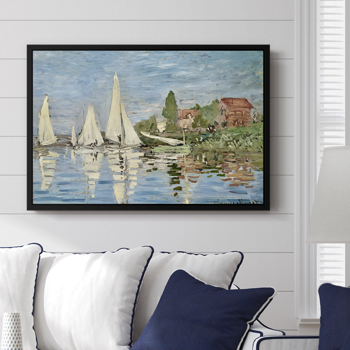 Regatta at Argenteuil, 1872 by Claude Monet displayed above a sofa in a living room in a black floater frame, featuring a lively regatta scene with multiple boats and fluttering sails.