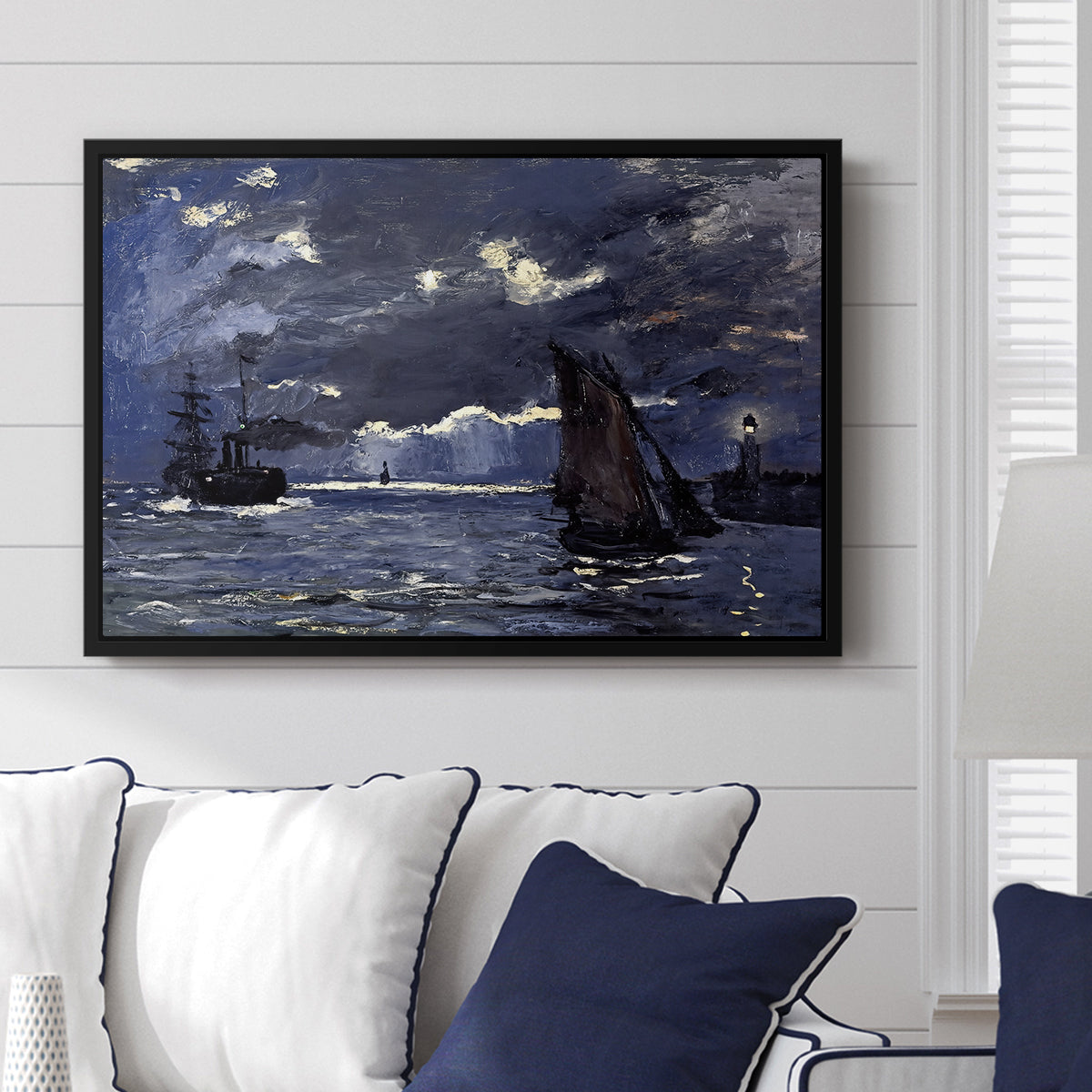A Seascape, Shipping by Moonlight, 1864 by Claude Monet displayed above a sofa in a living room in a black floater frame, featuring a nocturnal seascape with boats silhouetted against glowing moon.