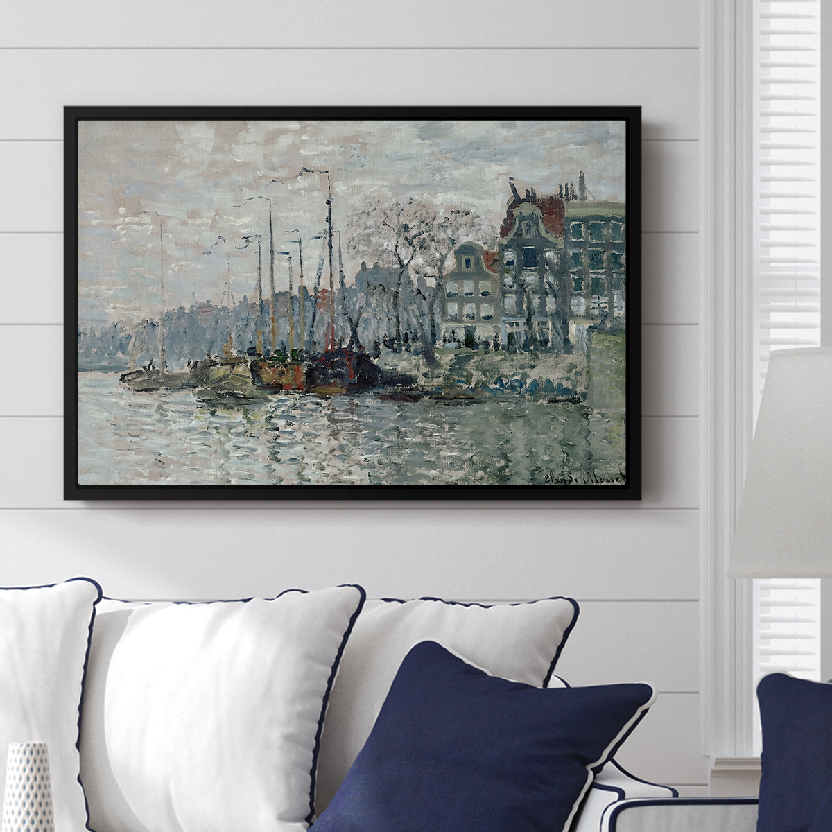 View of the Prins Hendrikkade and Kromme Waal in Amsterdam, 1874 by Claude Monet displayed above a sofa in a living room in a black floater frame, featuring an impressionist cityscape of canal with ships and architecture.