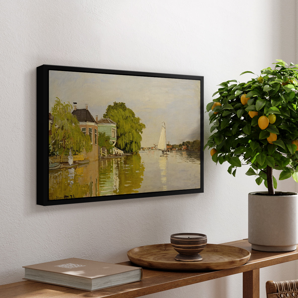 Houses on the Achterzaan, 1871 by Claude Monet, presented in a black floater framed canvas featuring colorful houses reflected in calm river surrounded by greenery, displayed above a hallway console table.