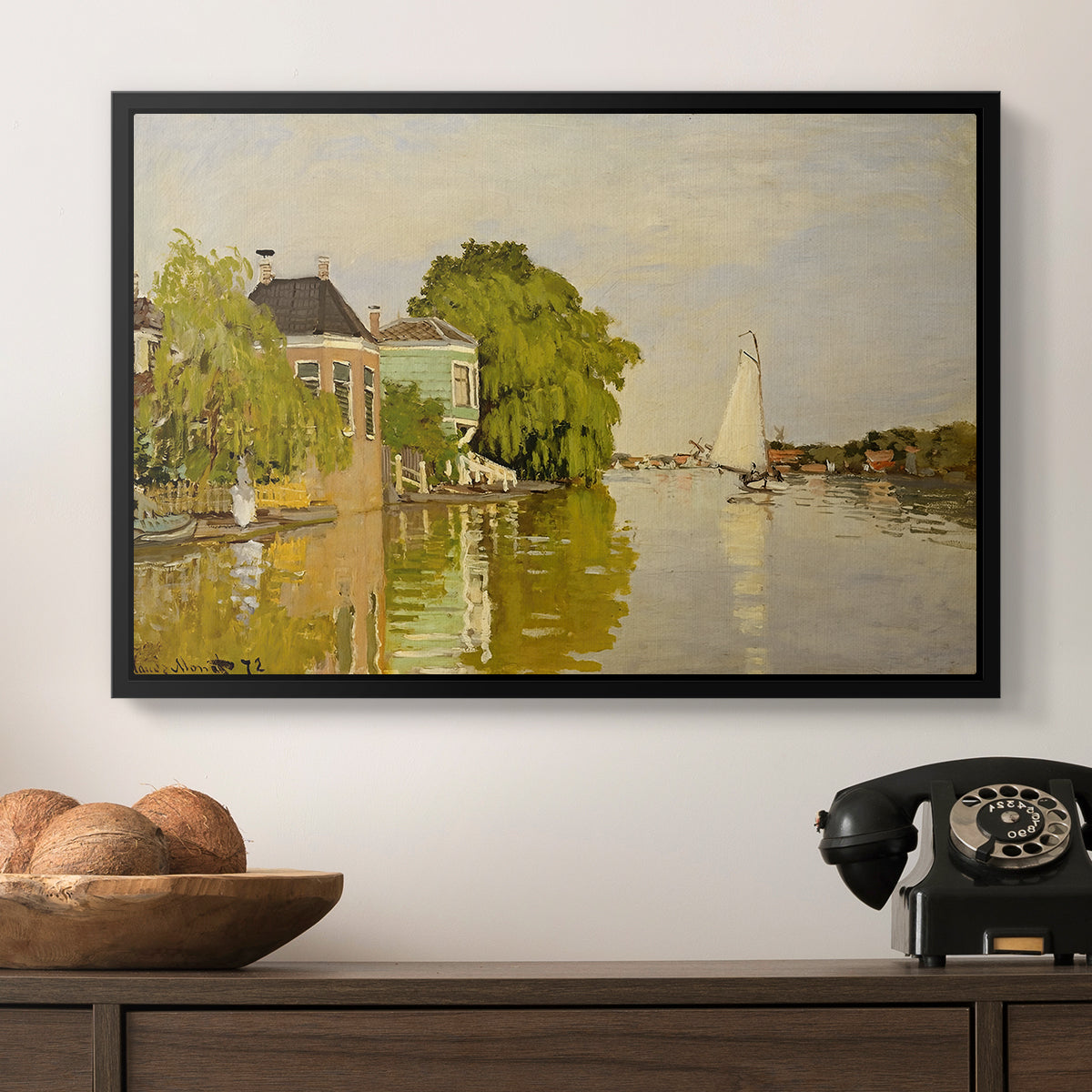 Houses on the Achterzaan, 1871 by Claude Monet in a black floater framed canvas displayed above a console table in a hallway, featuring a peaceful village scene with houses bordering water.
