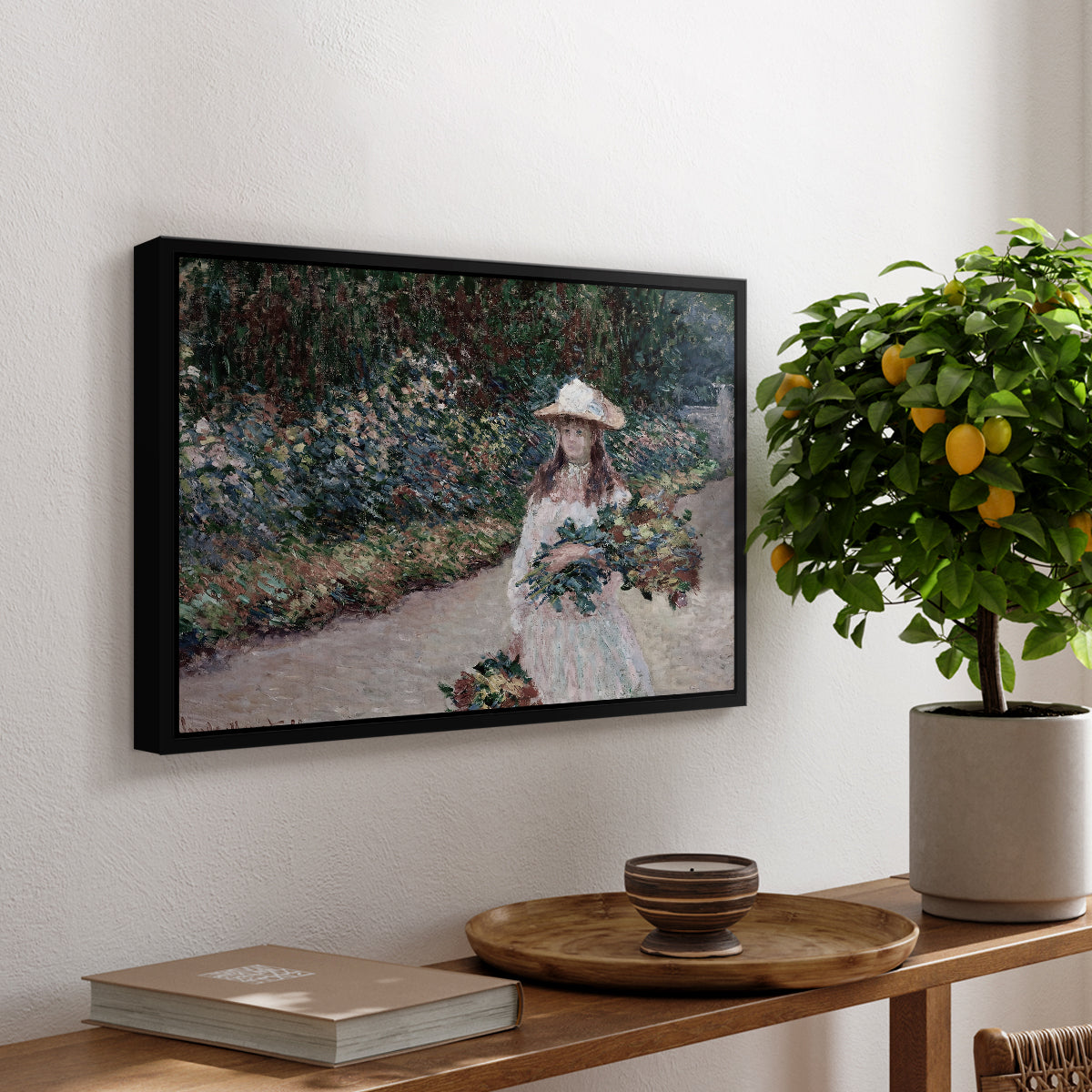 Young Girl in the Garden at Giverny, 1888 by Claude Monet, presented in a black floater framed canvas featuring a young girl seated in lush garden surrounded by blooming flowers, displayed above a hallway console table.