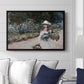 Young Girl in the Garden at Giverny, 1888 by Claude Monet displayed above a sofa in a living room in a black floater frame, featuring an impressionist garden scene with child among greenery and blossoms.