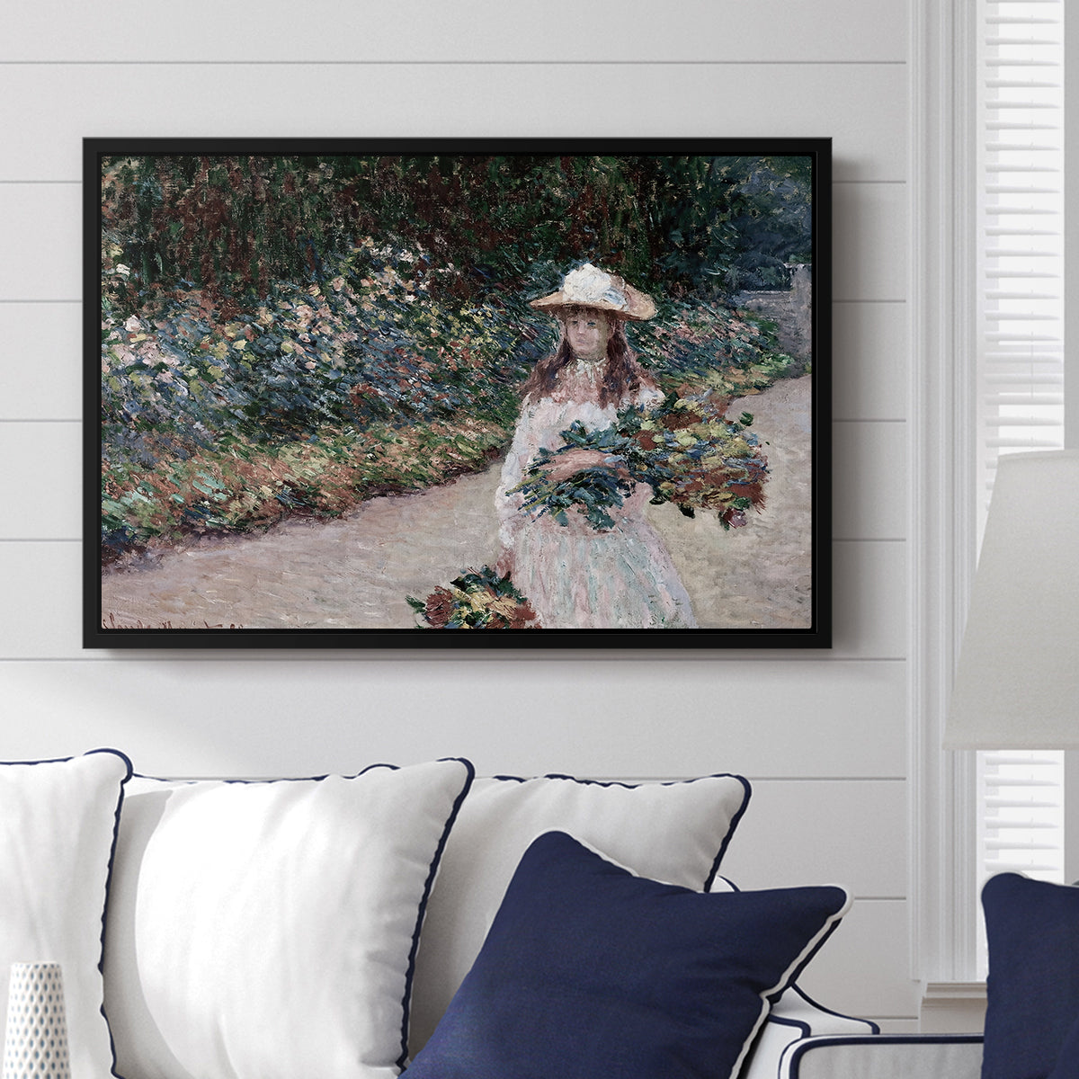 Young Girl in the Garden at Giverny, 1888 by Claude Monet displayed above a sofa in a living room in a black floater frame, featuring an impressionist garden scene with child among greenery and blossoms.