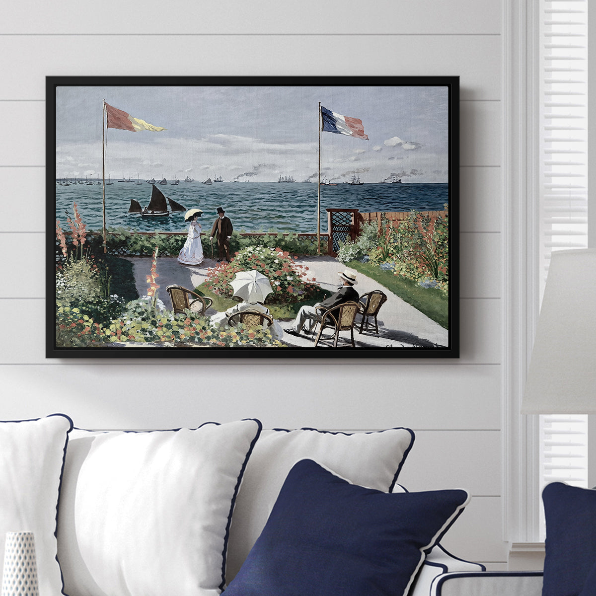 Garden at Sainte-Adresse, 1867 by Claude Monet displayed above a sofa in a living room in a black floater frame, featuring an impressionist coastal garden with people and ocean view.