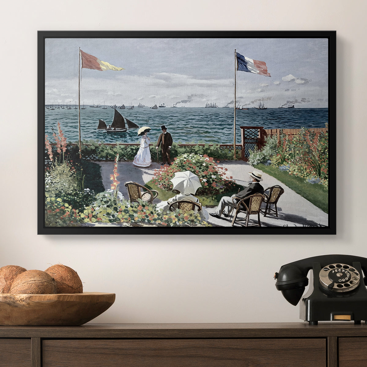 Garden at Sainte-Adresse, 1867 by Claude Monet in a black floater framed canvas displayed above a console table in a hallway, featuring a landscaped terrace with figures and flags near shoreline.