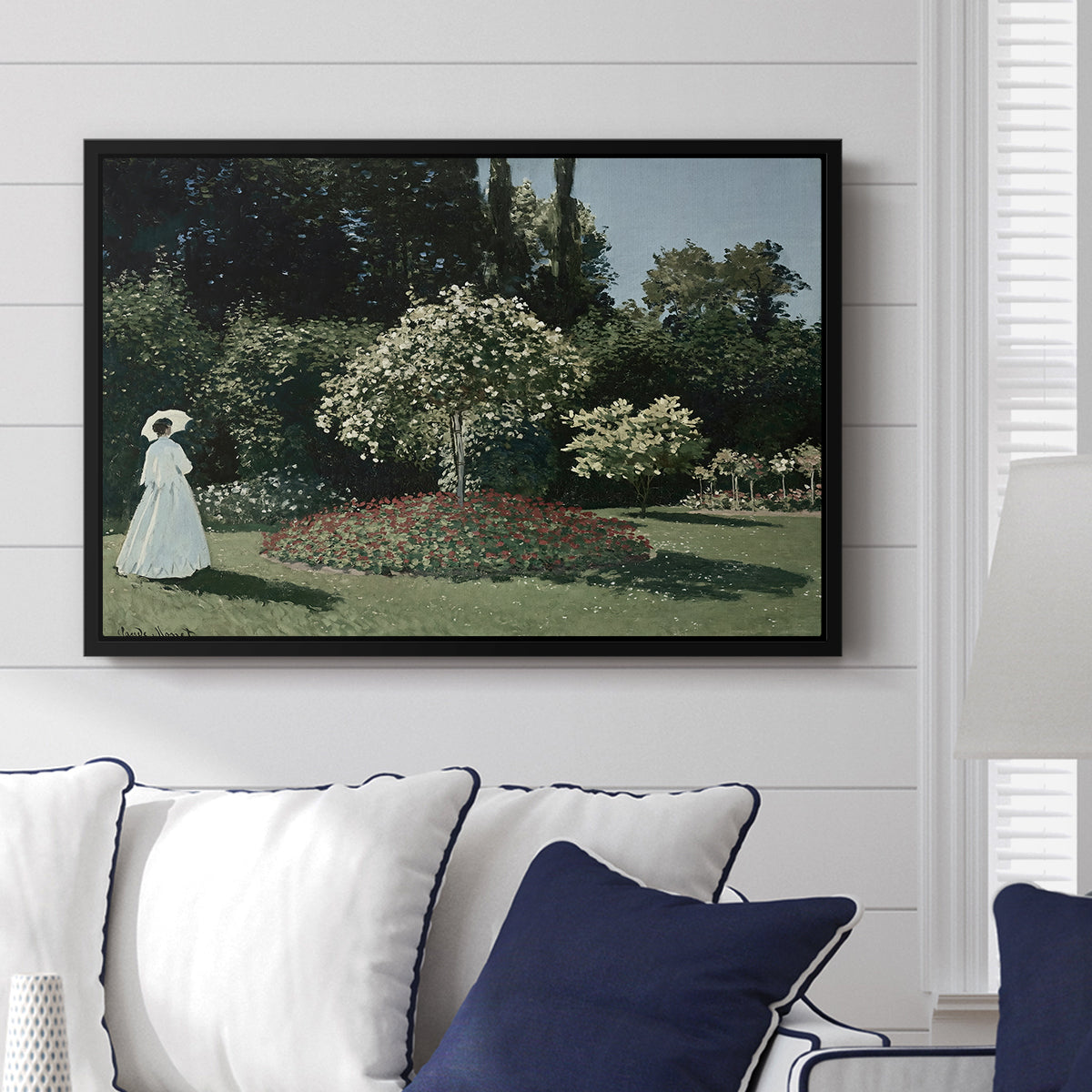 Woman in the Garden, Sainte-Adresse, 1867 by Claude Monet displayed above a sofa in a living room in a black floater frame, featuring an impressionist figure in sunlit garden with lush vegetation.
