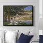 On the Bank of the Seine, Bennecourt, 1868 by Claude Monet displayed above a sofa in a living room in a black floater frame, featuring a peaceful riverside scene with figures resting in grassy area by water.