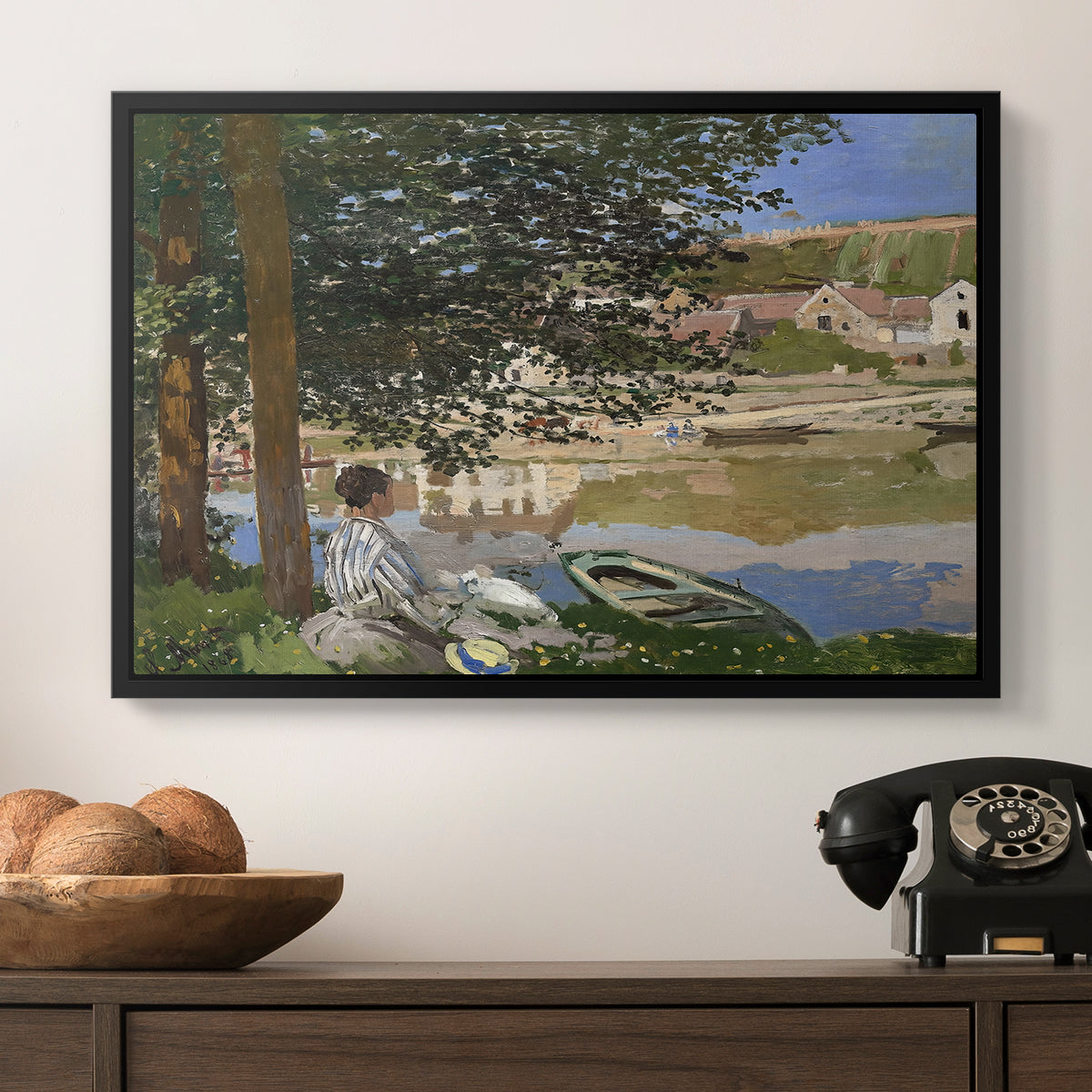 On the Bank of the Seine, Bennecourt, 1868 by Claude Monet in a black floater framed canvas displayed above a console table in a hallway, featuring a quiet outdoor setting with figures near river under foliage.