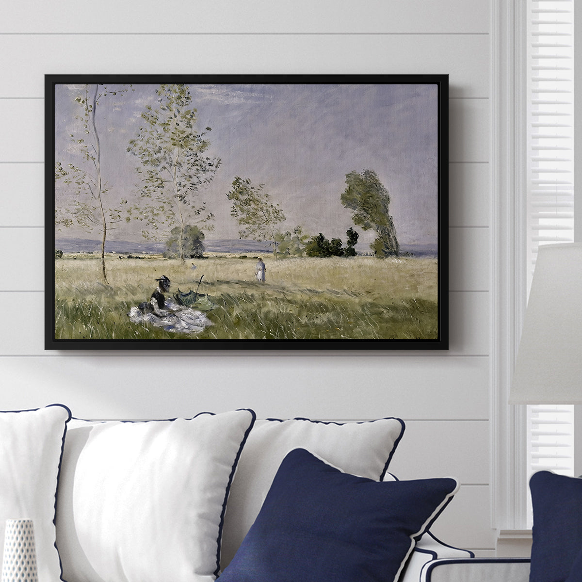 Summer (L'ete), 1874 by Claude Monet displayed above a sofa in a living room in a black floater frame, featuring an impressionist countryside scene with figure resting in shade.