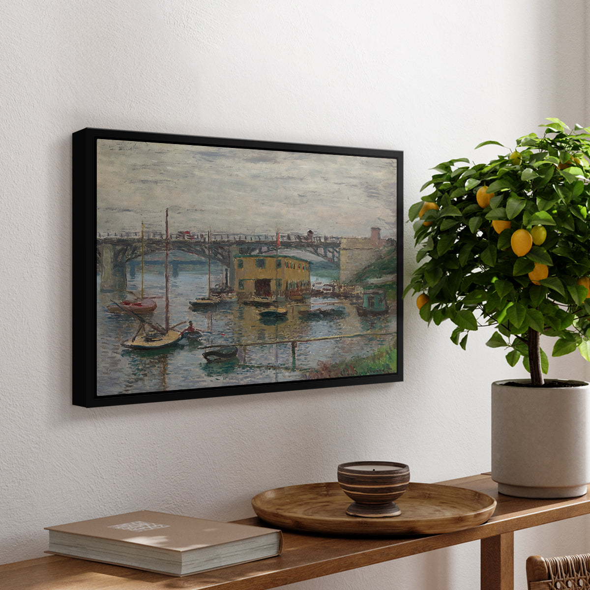 Bridge at Argenteuil on a Gray Day, c. 1876 by Claude Monet, presented in a black floater framed canvas featuring a bridge crossing river under gray sky with muted reflections, displayed above a hallway console table.