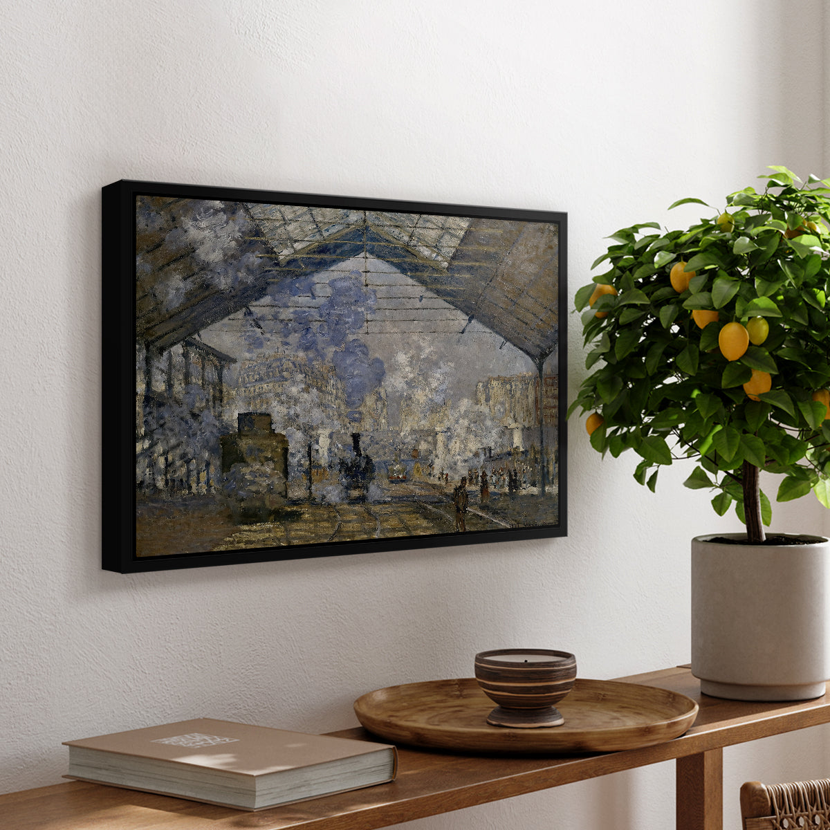 The Gare Saint-Lazare, 1877 by Claude Monet, presented in a black floater framed canvas featuring a train station interior filled with steam and locomotives under iron structure, displayed above a hallway console table.