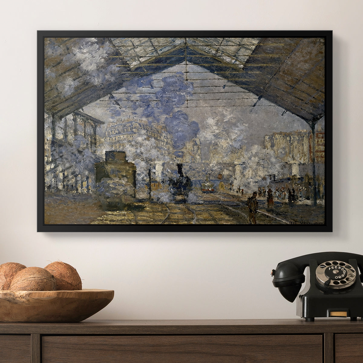 The Gare Saint-Lazare, 1877 by Claude Monet in a black floater framed canvas displayed above a console table in a hallway, featuring a bustling transport hub with trains beneath glass roof.