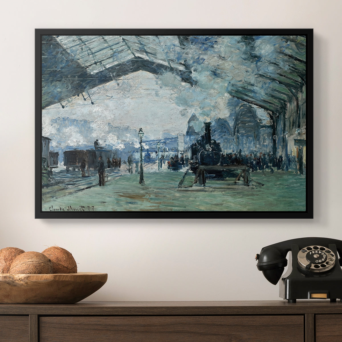 The Saint-Lazare Station, 1877 by Claude Monet in a black floater framed canvas displayed above a console table in a hallway, featuring a dramatic depiction of industrial space with trains and light.