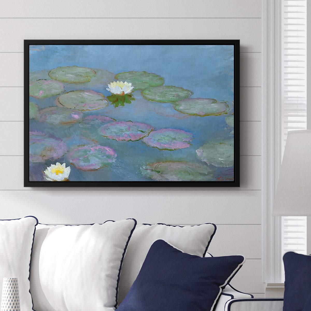 Water Lilies (Nymphéas), 1897-1899 by Claude Monet displayed above a sofa in a living room in a black floater frame, featuring an impressionist pond scene with lily pads and soft reflections.