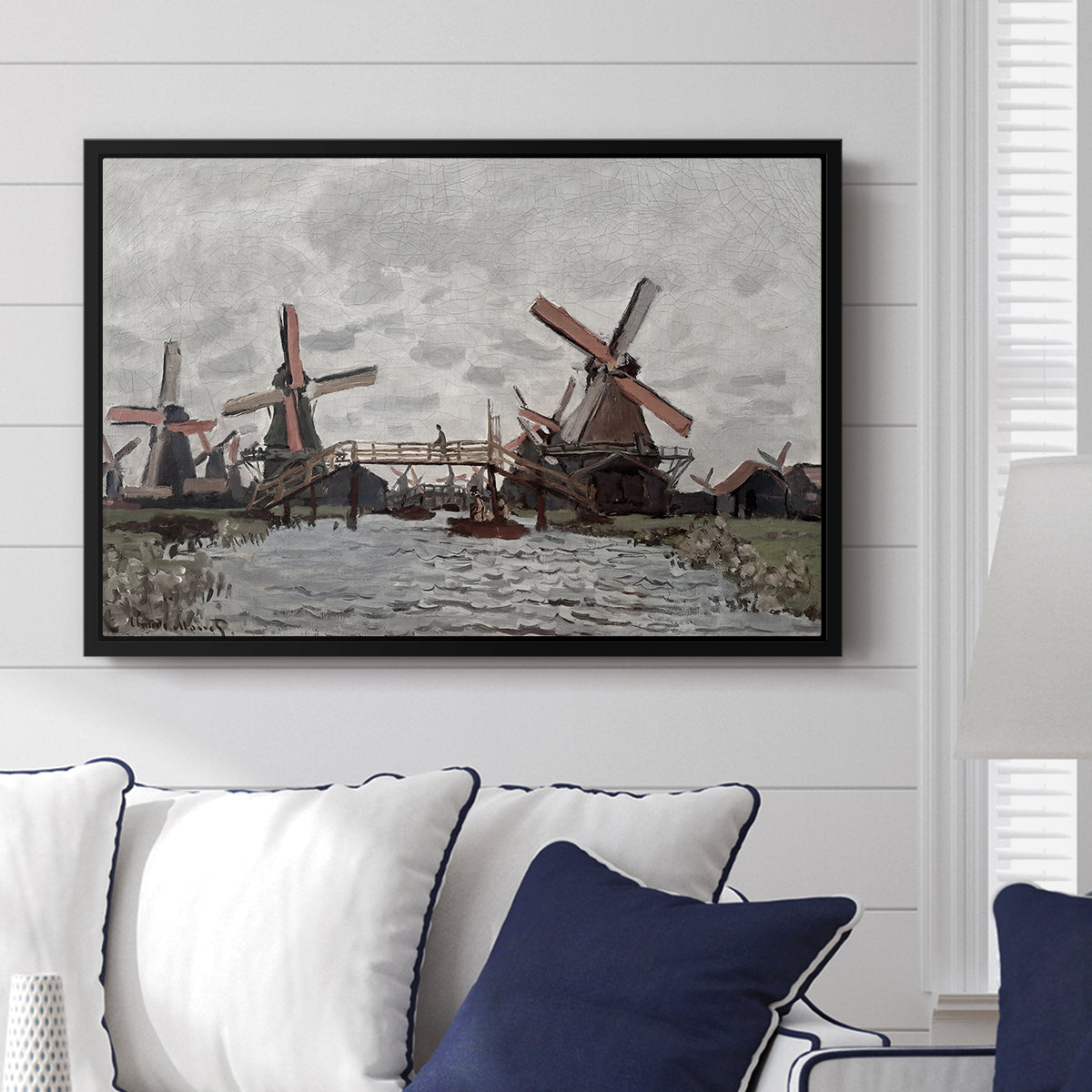 Windmills near Zaandam, 1871 by Claude Monet displayed above a sofa in a living room in a black floater frame, featuring an impressionist view of Dutch windmills along riverbank.