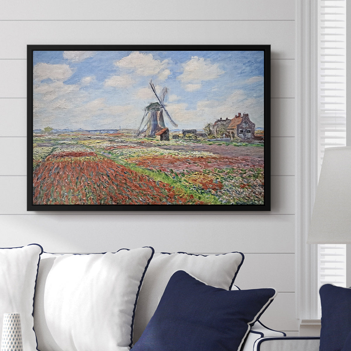 Tulip Fields with the Rijnsburg Windmill, 1886 by Claude Monet displayed above a sofa in a living room in a black floater frame, featuring a vibrant agricultural landscape with flowers and windmill.