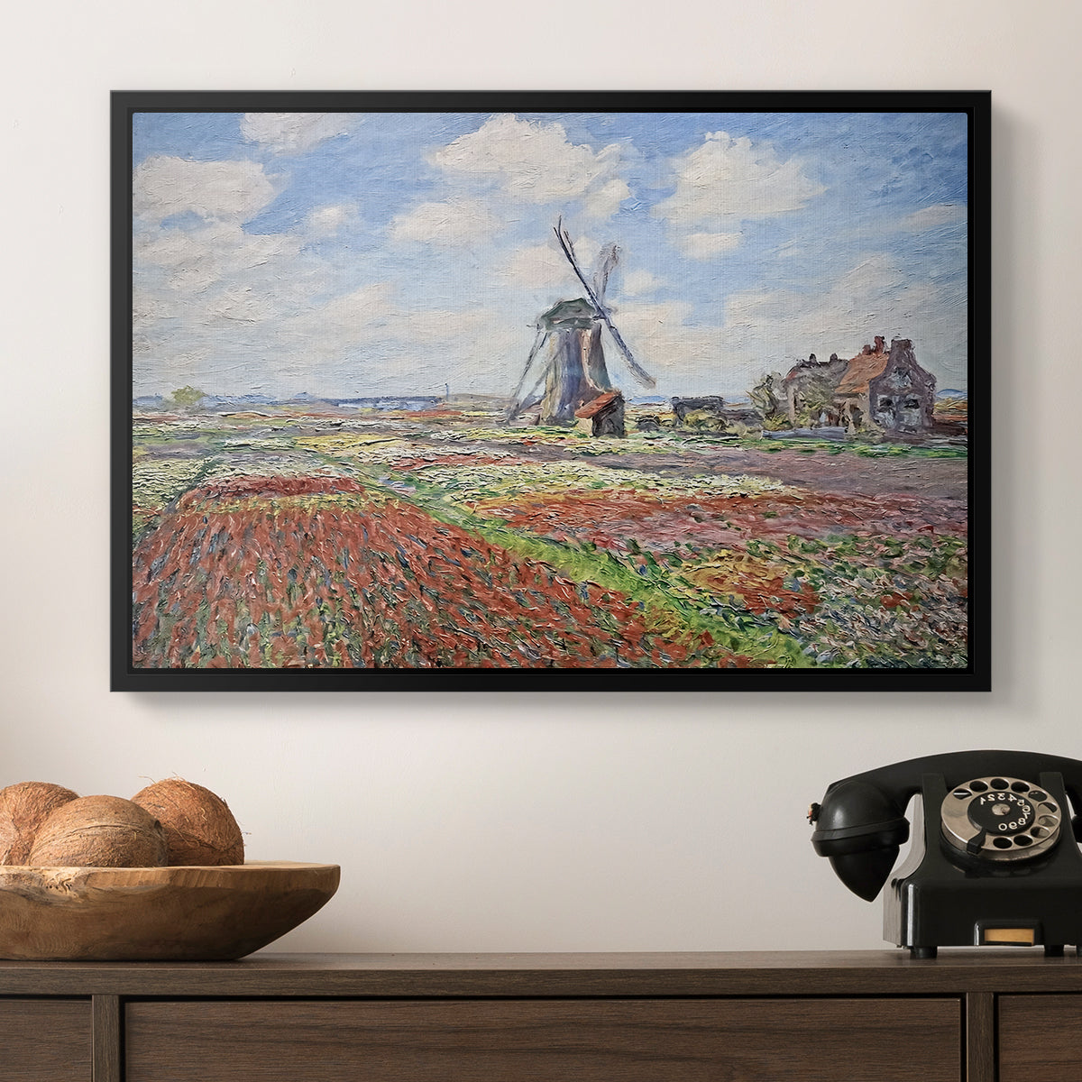 Tulip Fields with the Rijnsburg Windmill, 1886 by Claude Monet in a black floater framed canvas displayed above a console table in a hallway, featuring a rural scene with patterned rows of flowers and windmill.